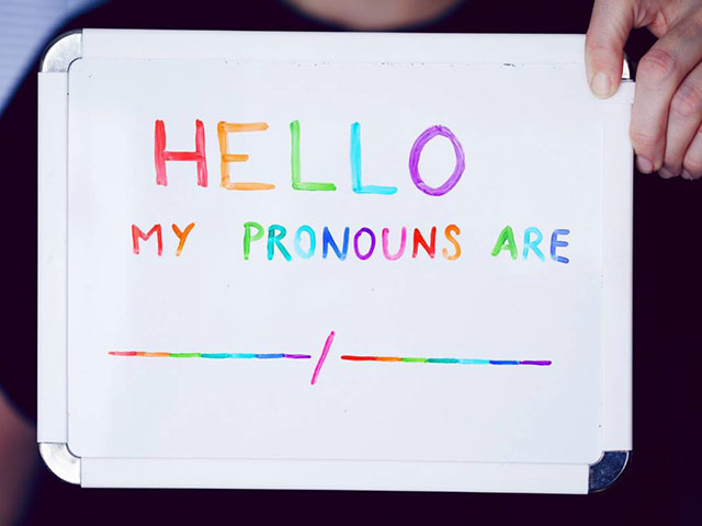 Persona tomando una pizarra blanca que dice 'Hello, my pronouns are' con letras de colores