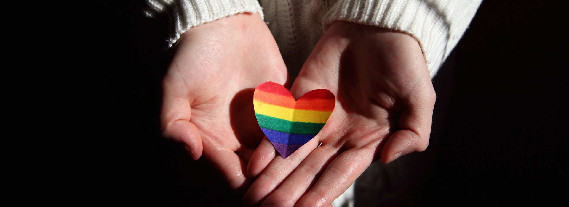 Manos abiertas de una persona tomando un corazón de papel arcoiris